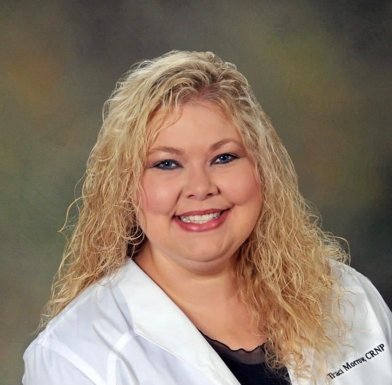  Traci Morrow smiles with long curly blonde hair in a white coat embroidered with her name.